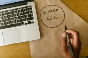Man with laptop writing LLC on paper and considering reasons Serbia is best for company formation