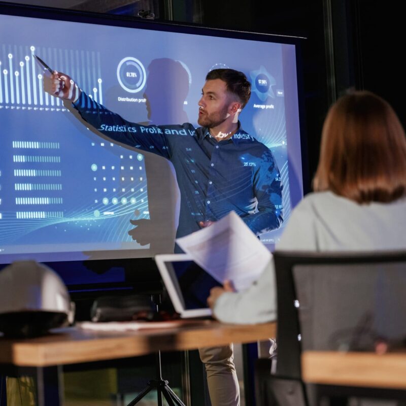 Helping to grow the company. Male business trainer is against projector with data, teaching people Helping to grow the company. Male business trainer is against projector with data, teaching people